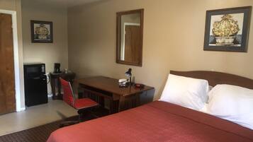 Quarto de hotel com uma cama, uma escrivaninha com cadeira, micro-ondas, cafeteira, relógio e um quadro na parede.