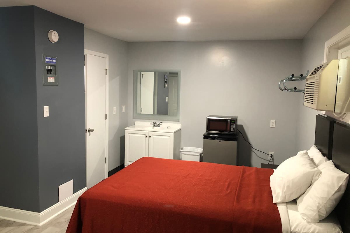 Quarto de hotel com cama, um pequeno espaço de cozinha, espelho e aquecedor fixado na parede.