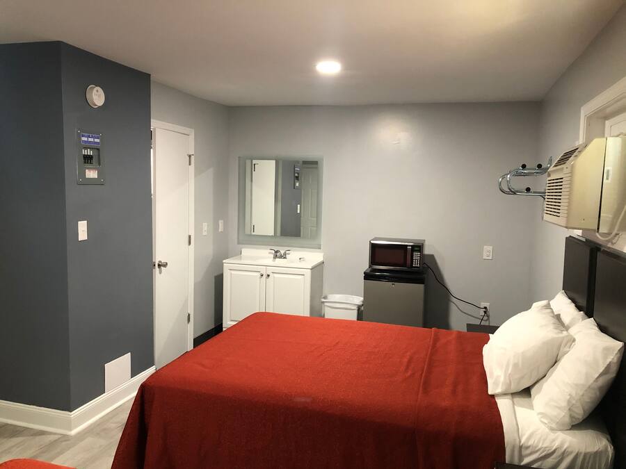 Una habitación de hotel con cama, kitchenette pequeña, espejo y calentador de pared.