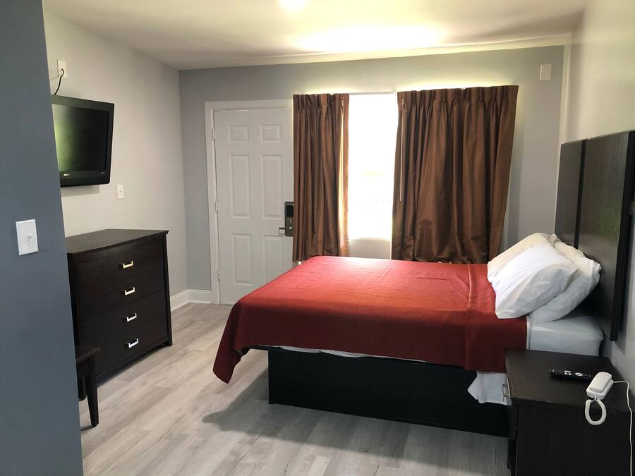 Un dormitorio con cama, cómoda, televisor, puerta y ventana con cortinas.