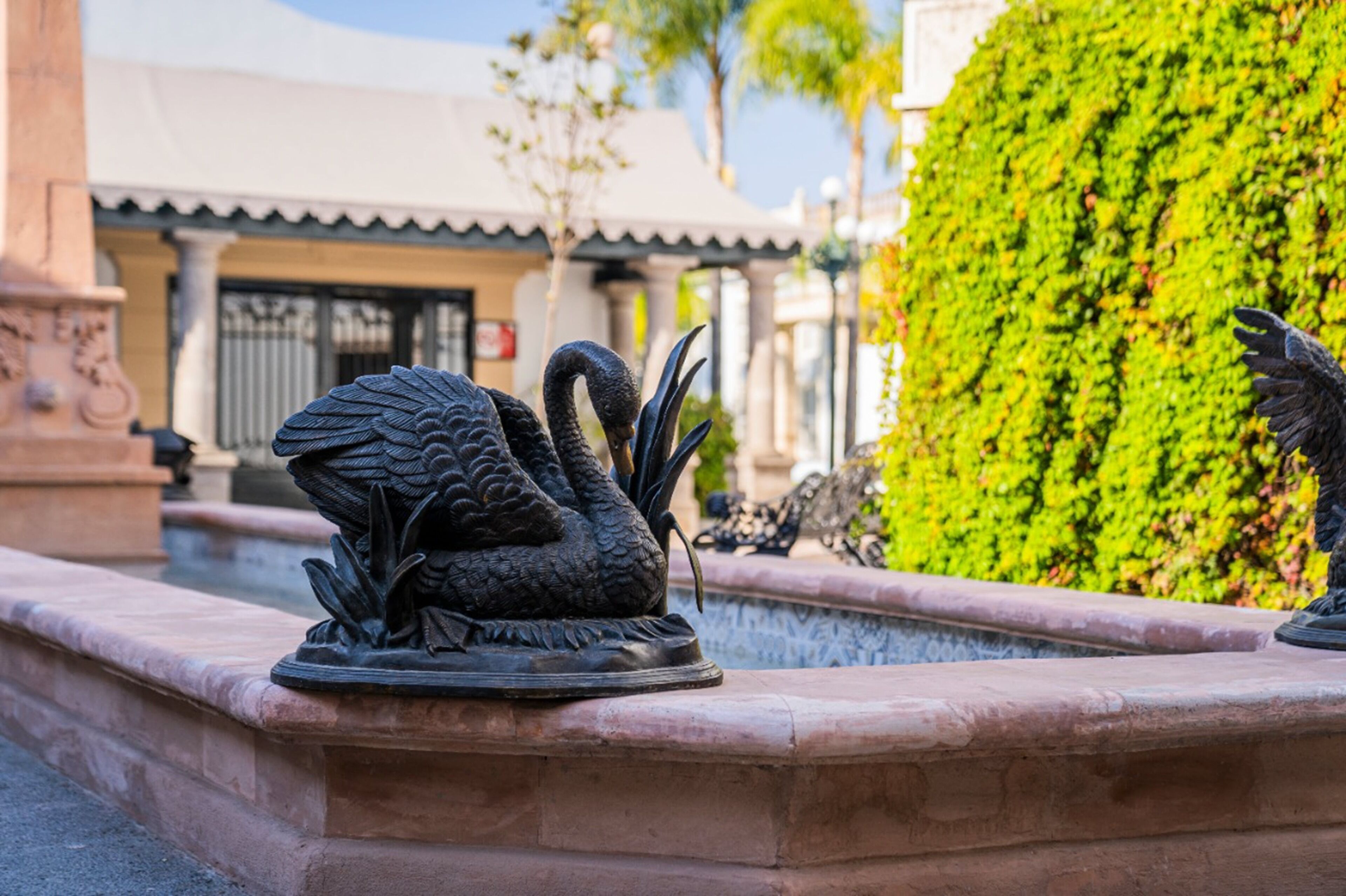 A statue of a swan on a fountain in a courtyard with a building in the background.