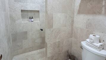 A bathroom with a shower, toilet, and a shelf with toiletries.