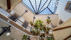 Un atrium de diversos nivells amb sostre de vidre, barana de ferro i plantes penjants.