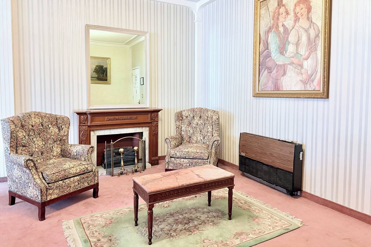 A room with two armchairs, a wooden coffee table, a fireplace, and a large framed painting on the wall.