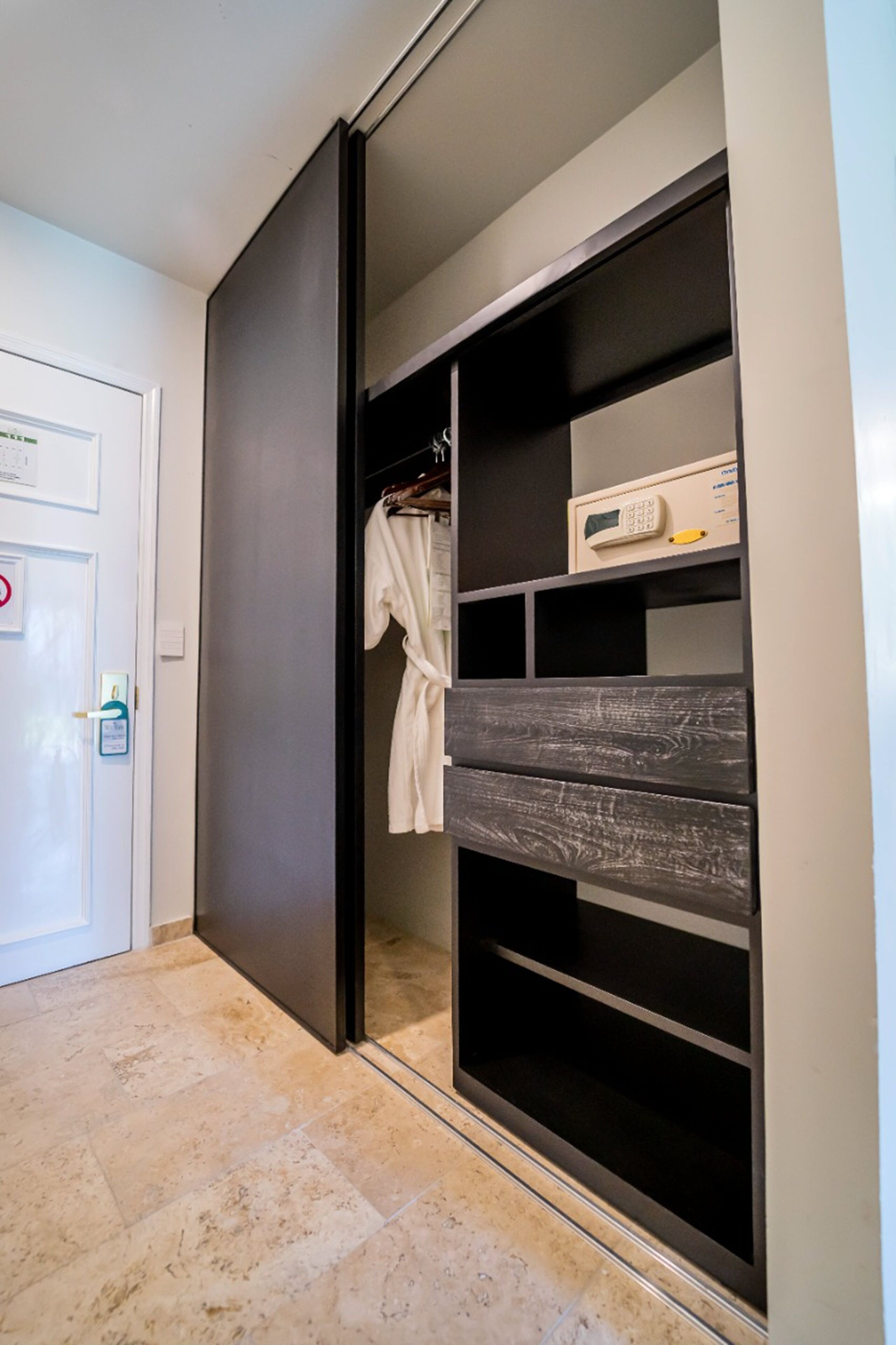 A modern closet with sliding doors, a robe hanging on a rack, and a small box on the top shelf.
