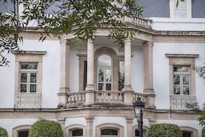 Fachada clásica de edificio con ventanas arqueadas, un balcón central con barandillas ornamentales y un diseño simétrico.