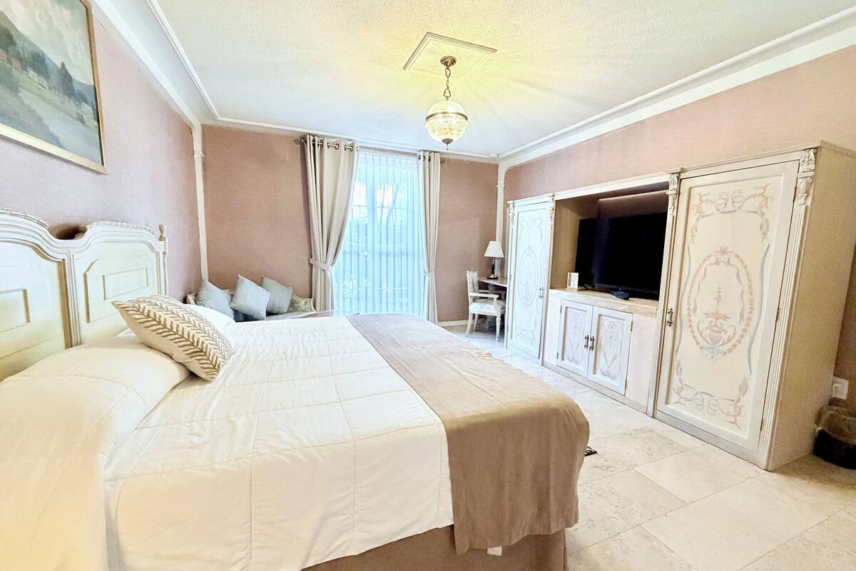 A bedroom with a large bed, a TV, a wardrobe, and a chandelier.