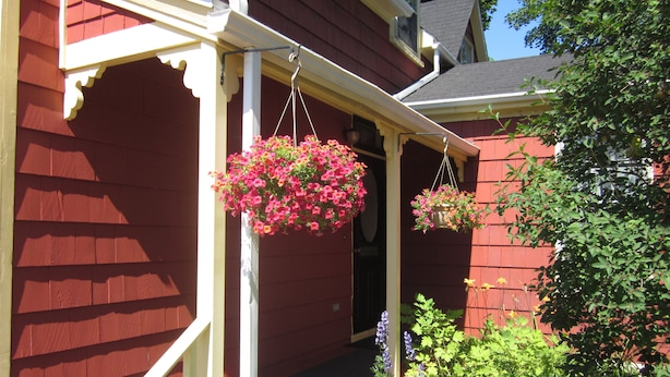 A red house with a porch and hanging flower baskets. - School Street House (Charlottetown)