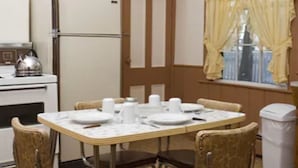 A dining area with a table set for four, surrounded by four chairs. There is a refrigerator and an oven in the background. - School Street House (Charlottetown)