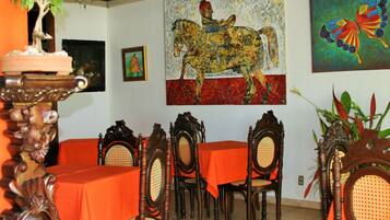 Un comedor con sillas y mesas de madera, un ventilador de techo y obras de arte en las paredes.