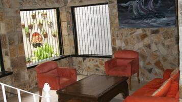 A room with stone walls, two red chairs, a wooden table, and a painting of a ship on the wall.