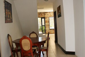 A dining area with a wooden table and chairs, a stone wall, and a door leading outside. - La Posada del Arcangel (Managua)