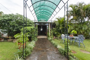 A stone pathway leading to a covered entrance, surrounded by lush greenery and a metal table with chairs. - La Posada del Arcangel (Managua)