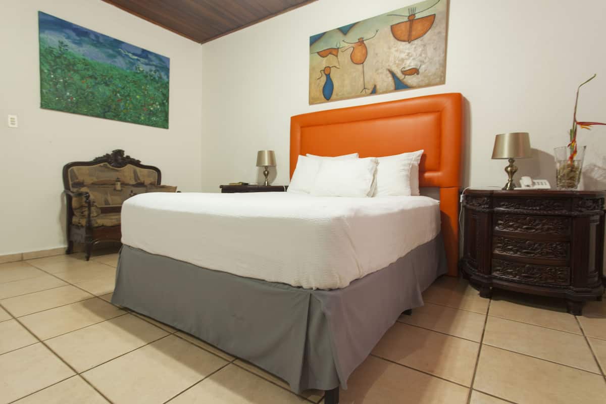 A bedroom with a large bed, a wooden nightstand, a dresser, and two paintings on the walls.