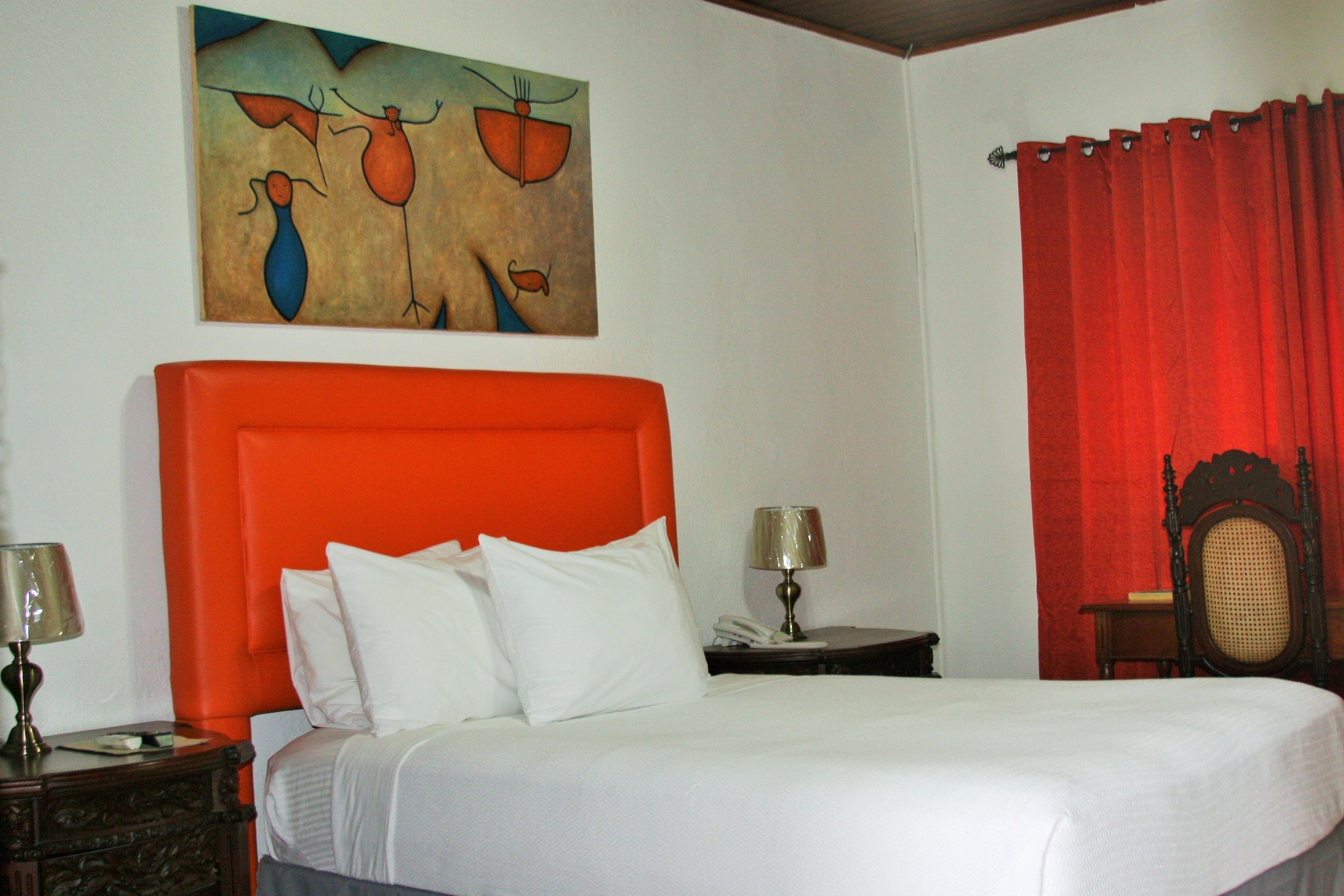 A hotel room with a large bed, a red headboard, and a painting on the wall.