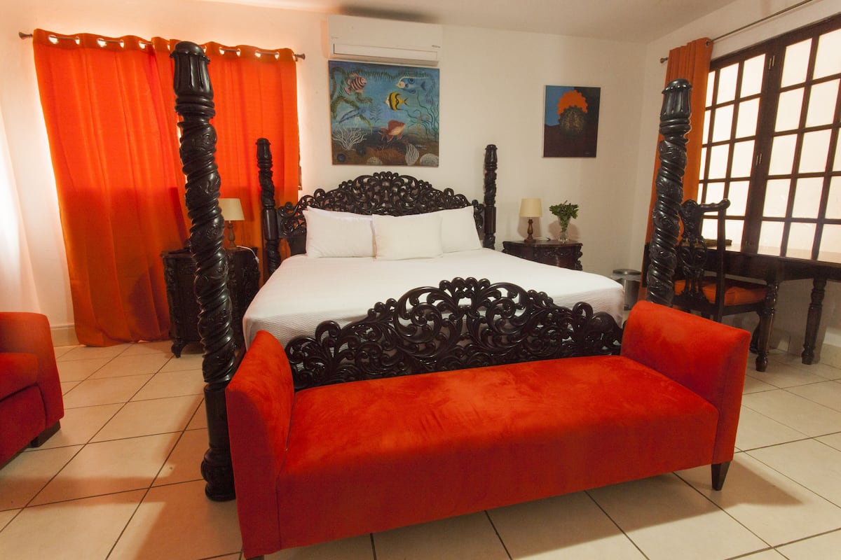 A bedroom with a large bed, a wooden headboard, a red sofa, and a window with curtains.