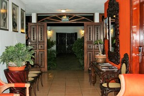 A hotel entrance with a sign reading "SALIDA," a tiled floor, wooden furniture, and potted plants. - La Posada del Arcangel (Managua)