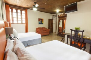 Una habitación de hotel con dos camas, un escritorio, una silla, un televisor y un ventilador de techo.