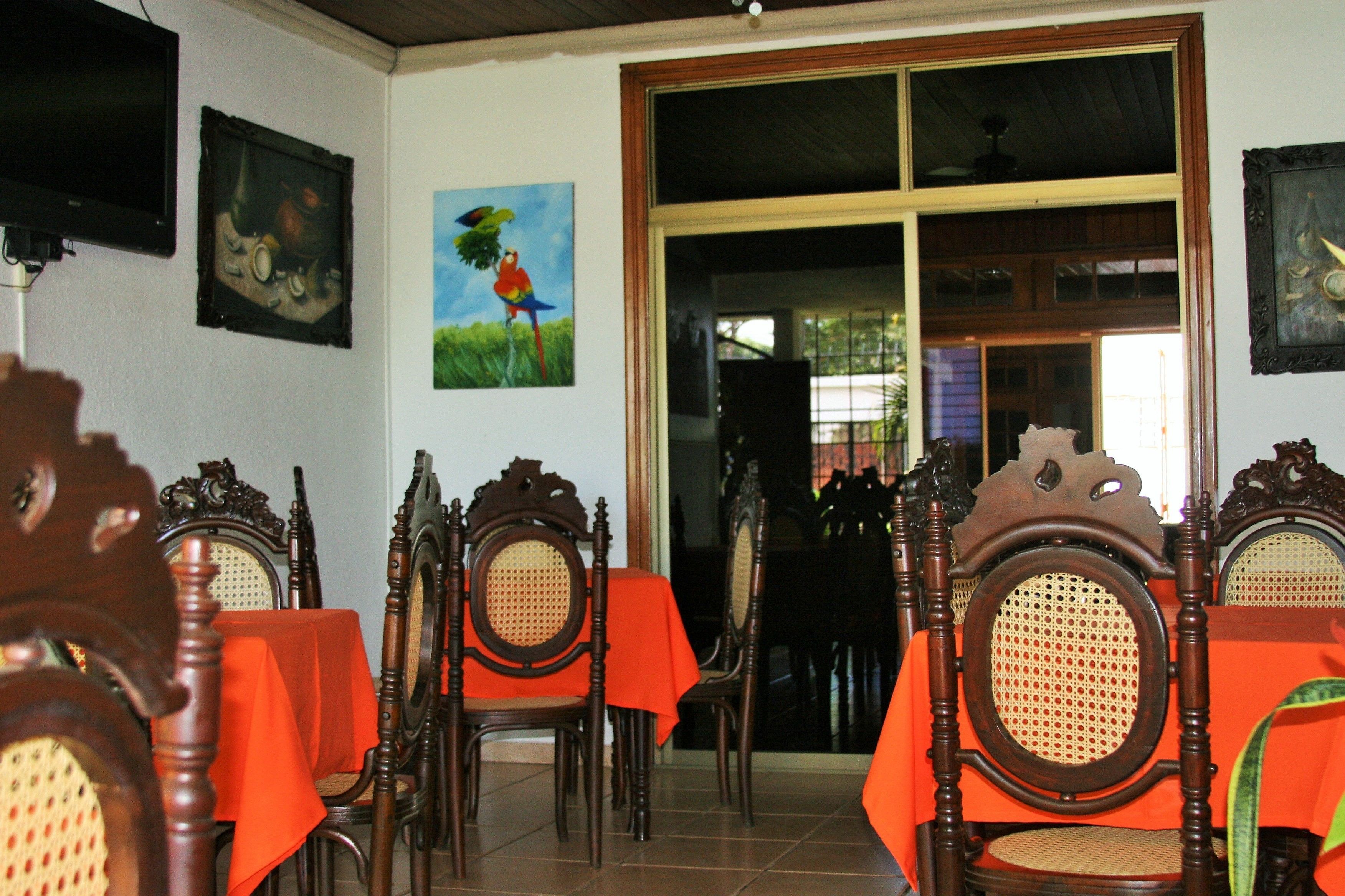 A dining area with wooden chairs and tables, some with orange tablecloths.