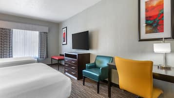 A hotel room with two beds, a desk with a chair, a television, and a painting on the wall.