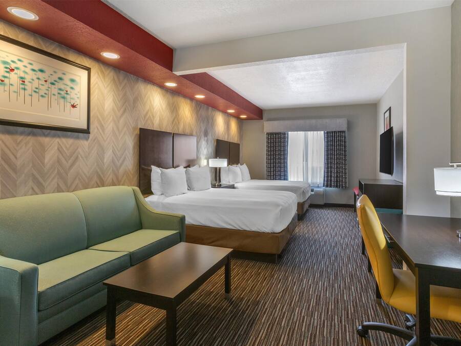 Une chambre d’hôtel avec un canapé, deux lits, un bureau et une télévision.