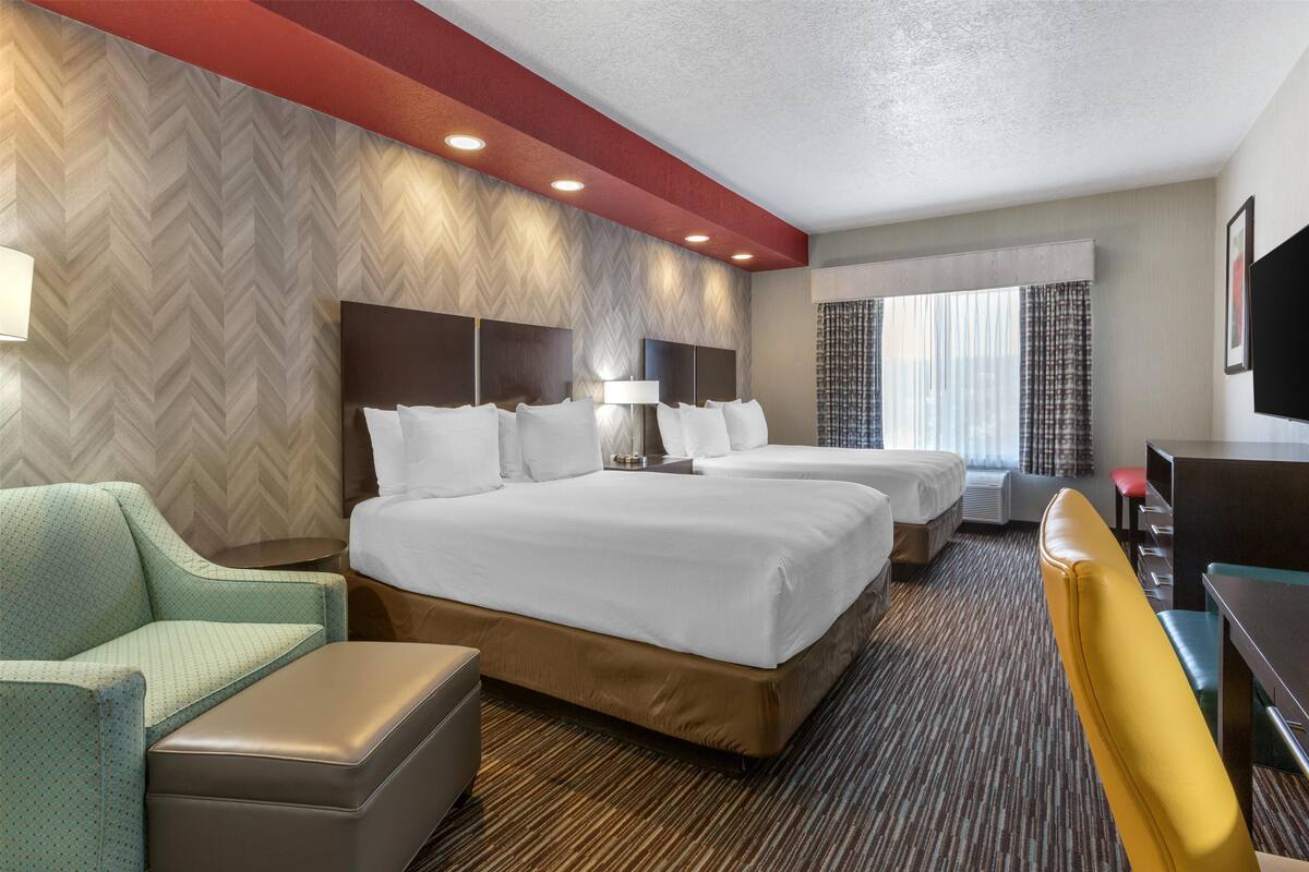 A hotel room with two beds, a sofa, a desk, and a TV.