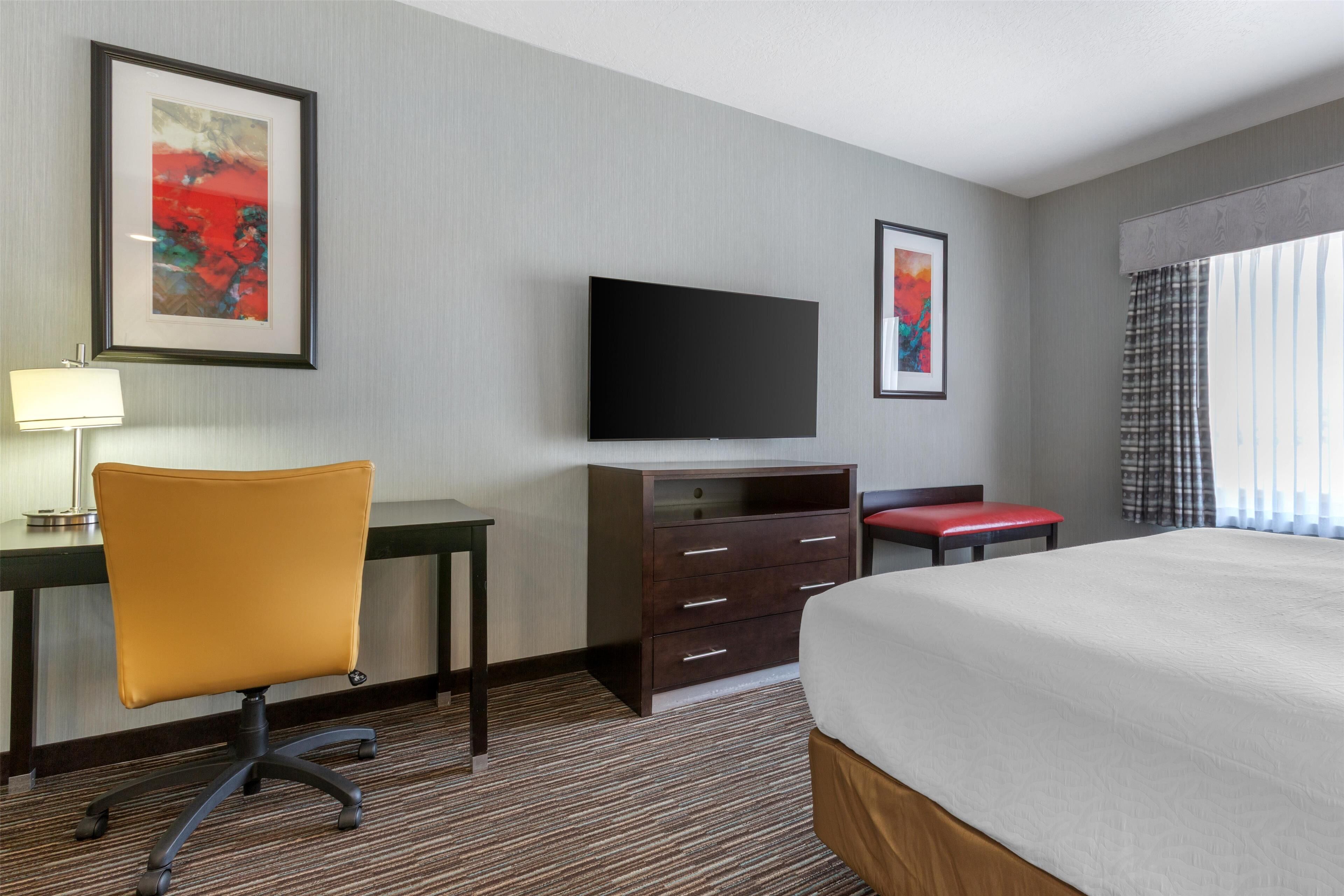 Una habitación de hotel con cama, escritorio, silla, televisor y cómoda.