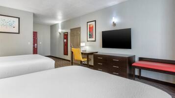 A hotel room with two beds, a desk with a chair, a TV, and a bench.