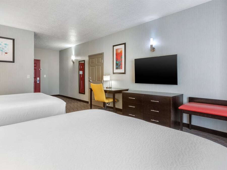 A hotel room with two beds, a desk with a chair, a TV, and a bench.