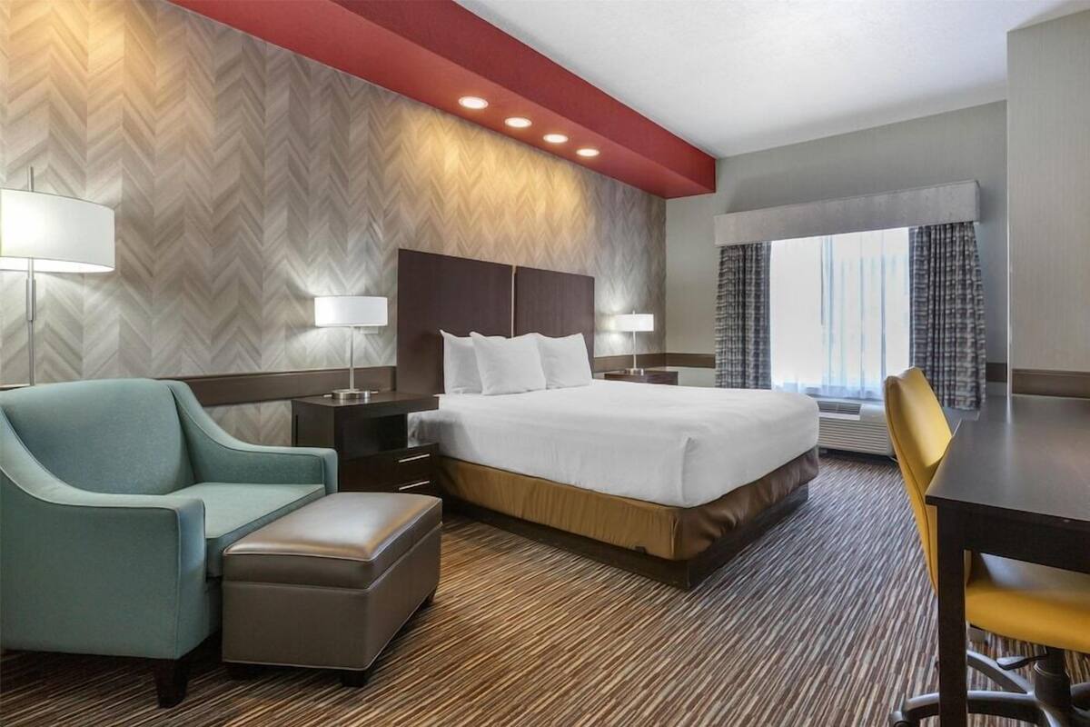 A hotel room with a large bed, a desk, a chair, a sofa, and a window with curtains.