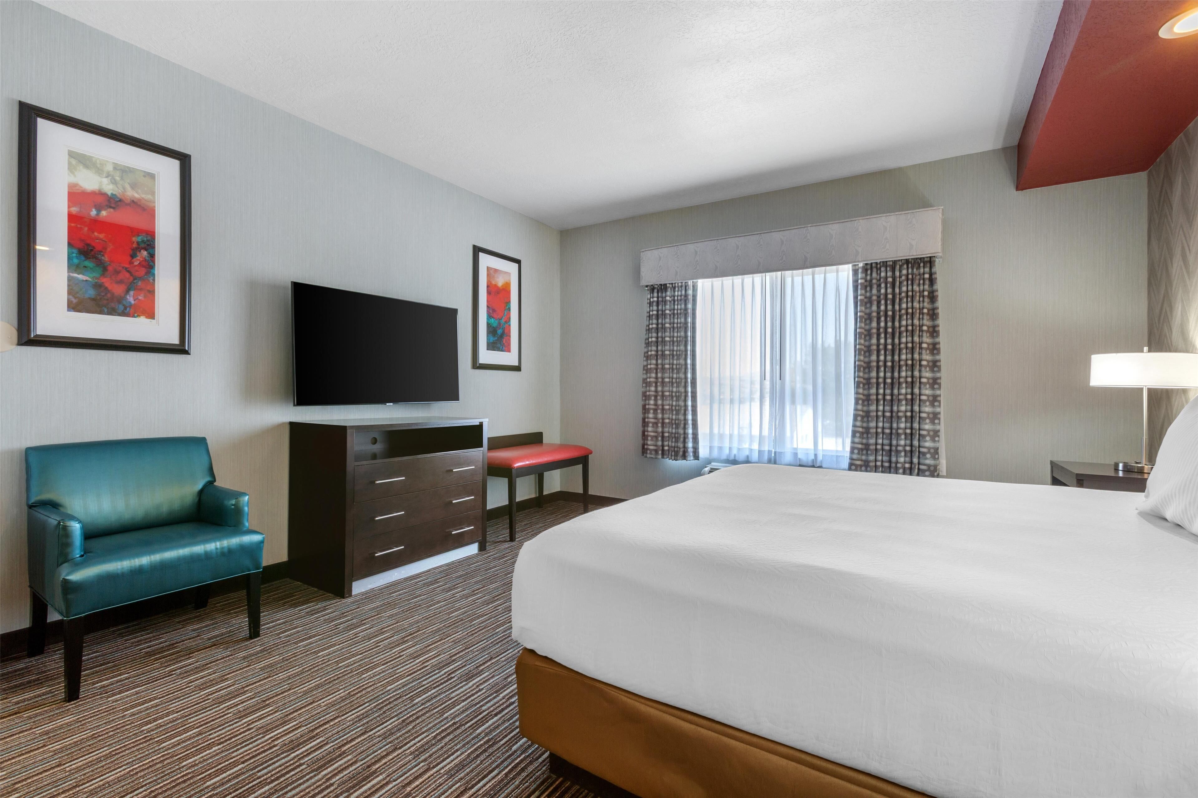 A hotel room with a large bed, a television, a desk, a chair, and two framed pictures on the wall.