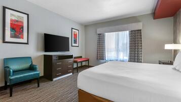 A hotel room with a large bed, a television, a desk, a chair, and two framed pictures on the wall.