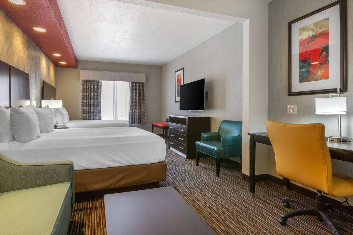 A hotel room with a large bed, a desk, a chair, a TV, and a painting on the wall.
