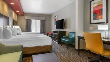 A hotel room with a large bed, a desk, a chair, a TV, and a painting on the wall.