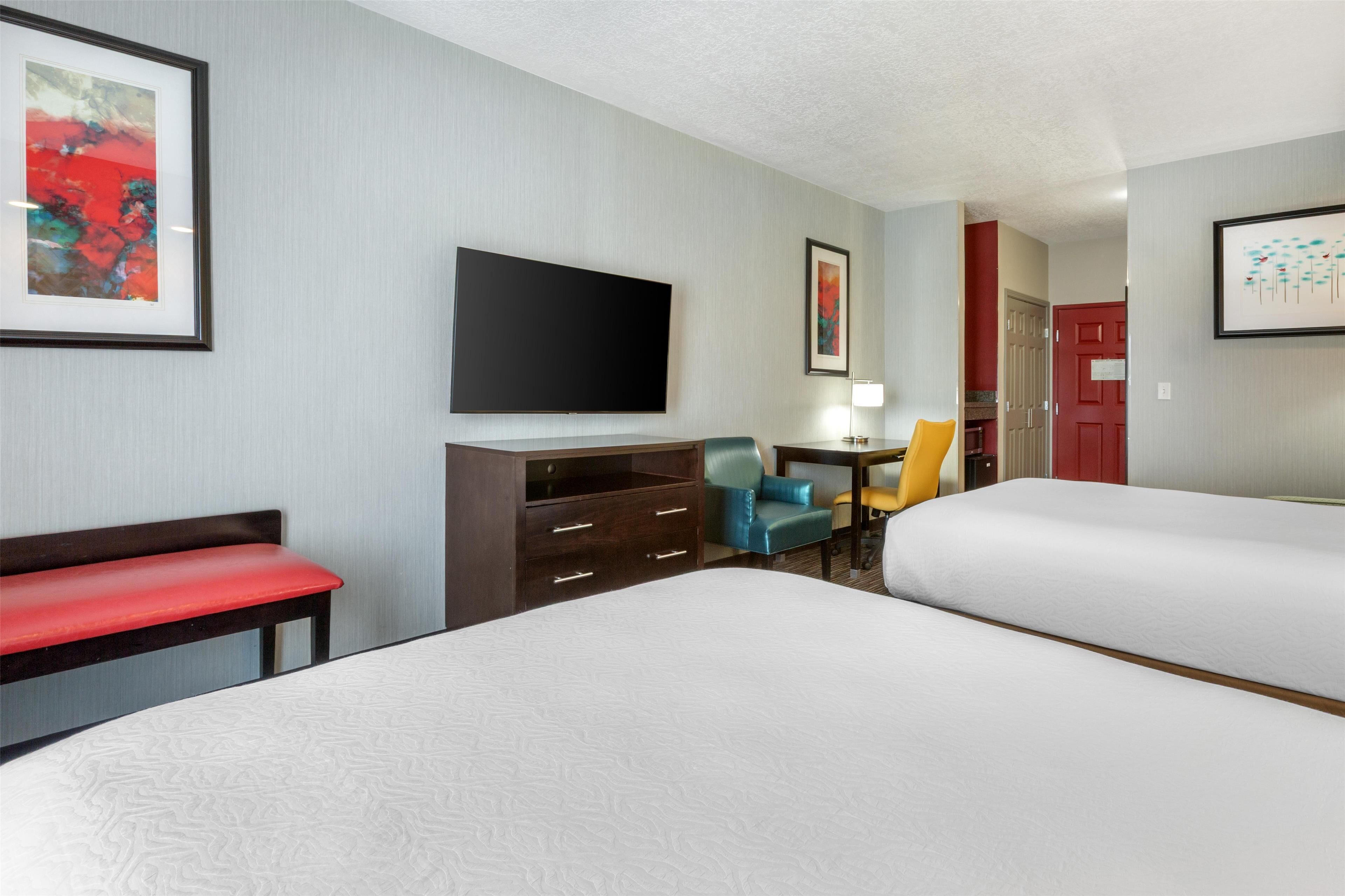 A hotel room with two beds, a desk, a chair, a TV, and artwork on the walls.