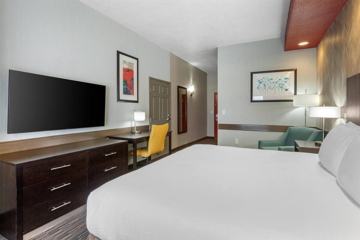 A hotel room with a large bed, a desk with a chair, a television, and two lamps.