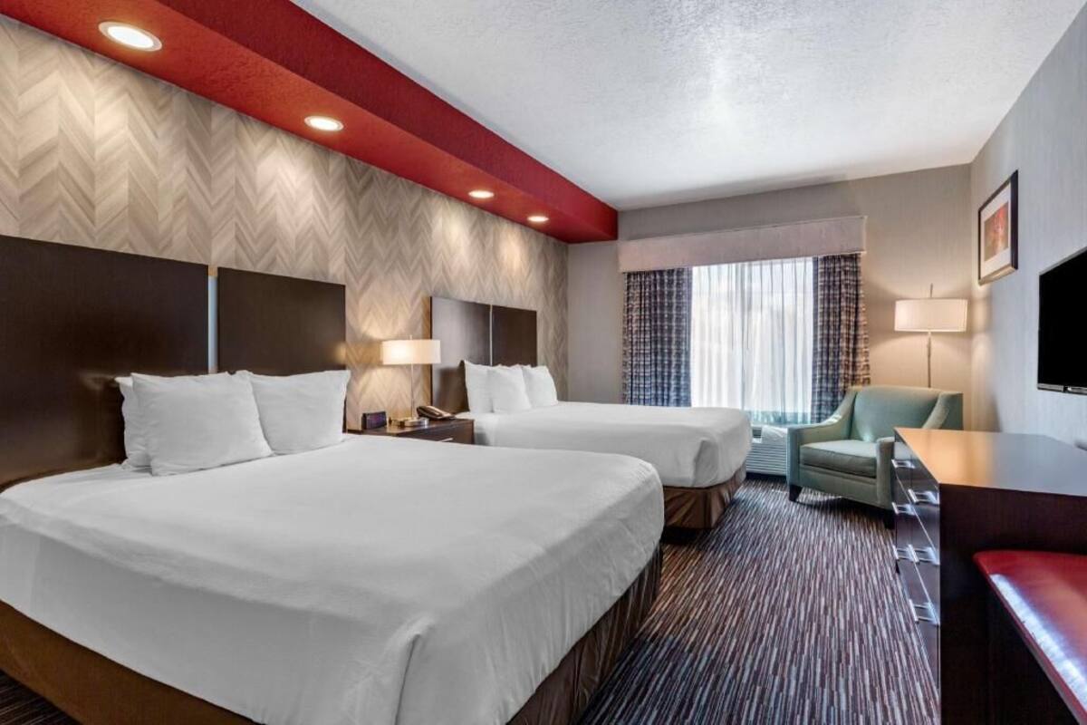 A hotel room with two beds, a desk, a chair, a TV, and a window with curtains.