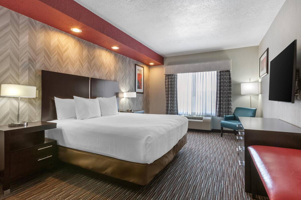 A hotel room with a large bed, a desk, a chair, and a window with curtains.