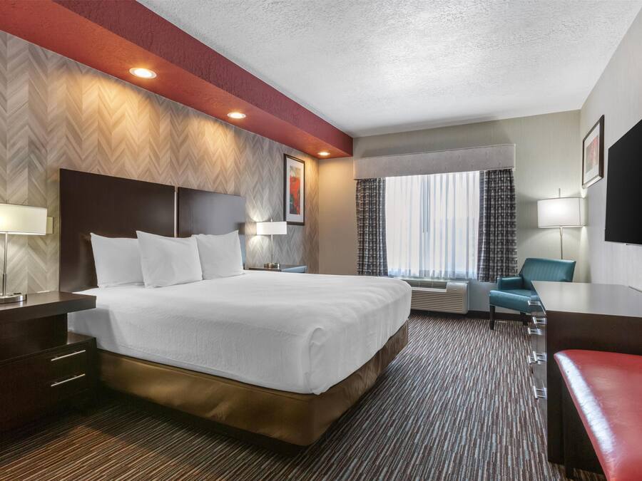 A hotel room with a large bed, a desk, a chair, and a window with curtains.