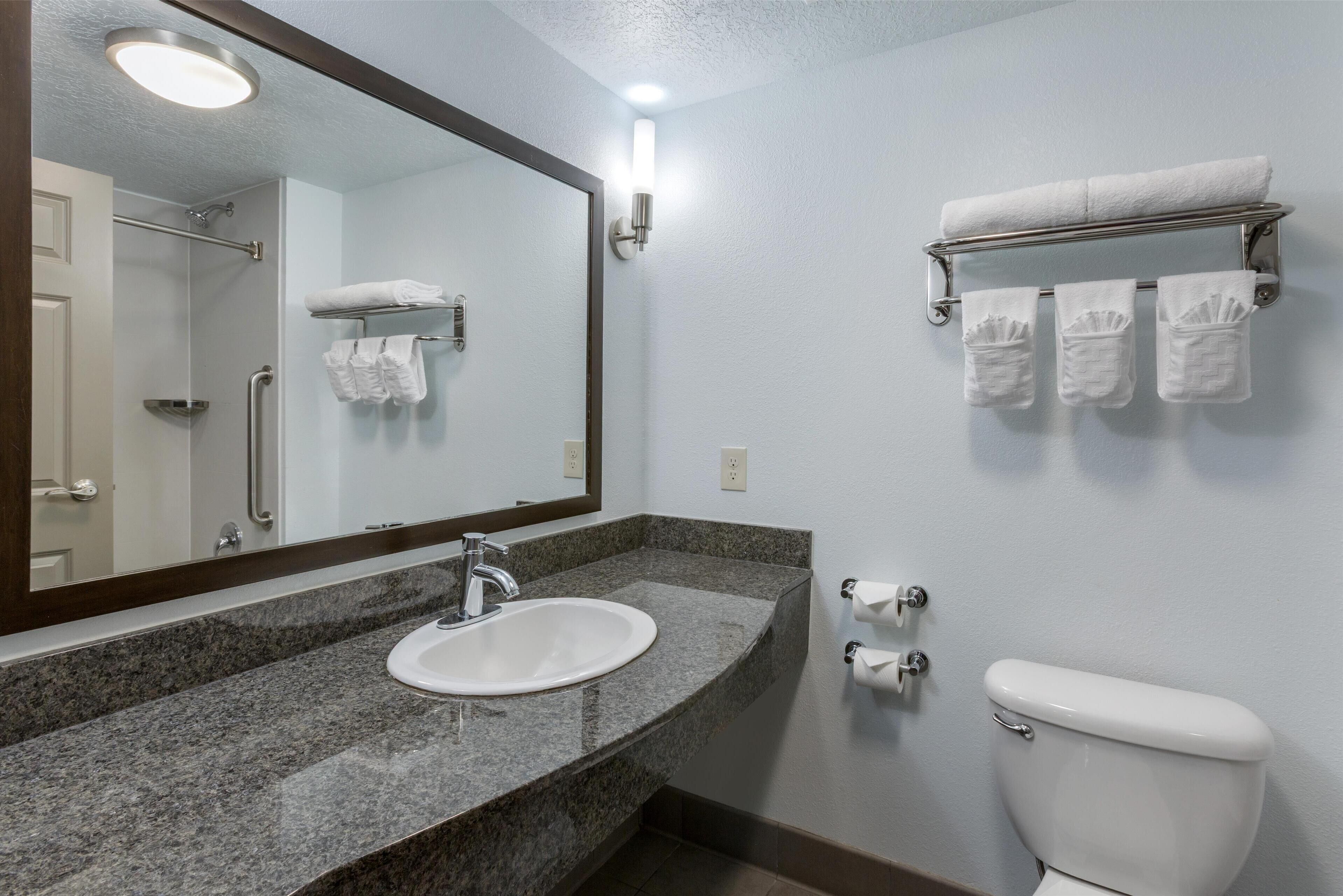 A bathroom with a granite countertop sink, a mirror, a towel rack with towels, and a toilet.