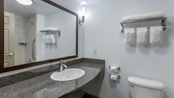 A bathroom with a granite countertop sink, a mirror, a towel rack with towels, and a toilet.