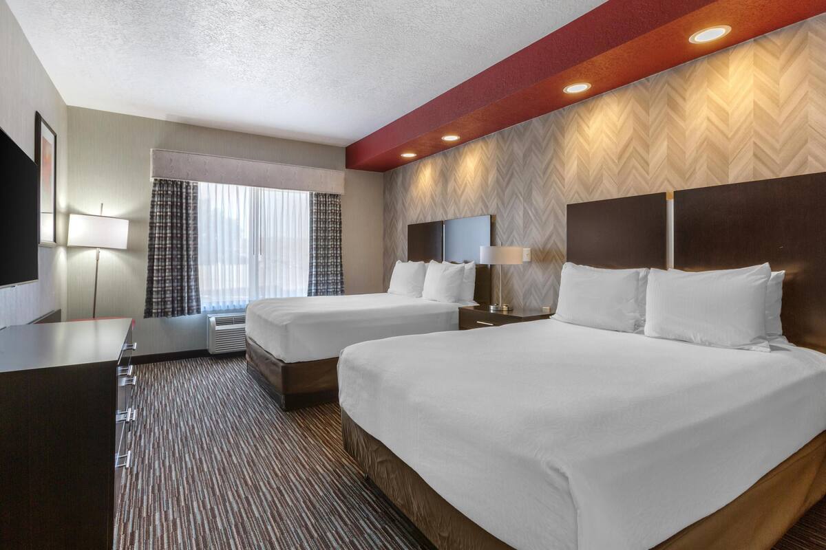 A hotel room with two beds, a desk, a TV, and a window with curtains.