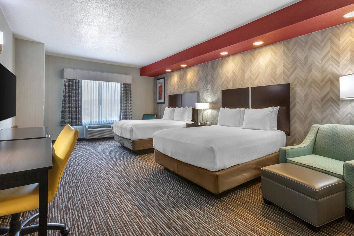 A hotel room with two beds, a desk, a chair, and a TV.