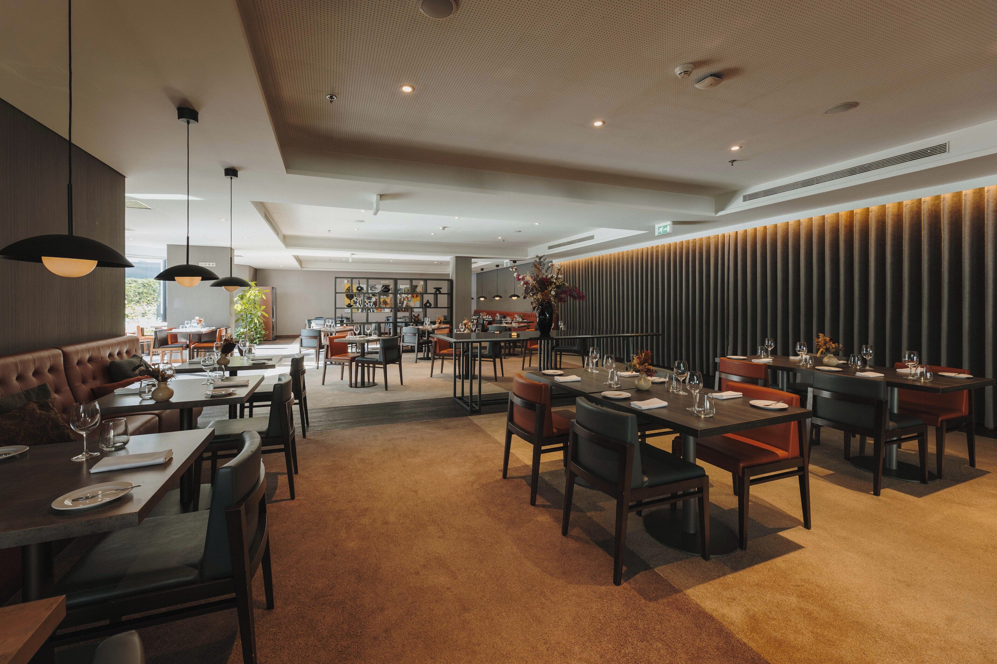 A modern restaurant with a mix of booth and table seating, a warm carpeted floor, and a contemporary ceiling design.