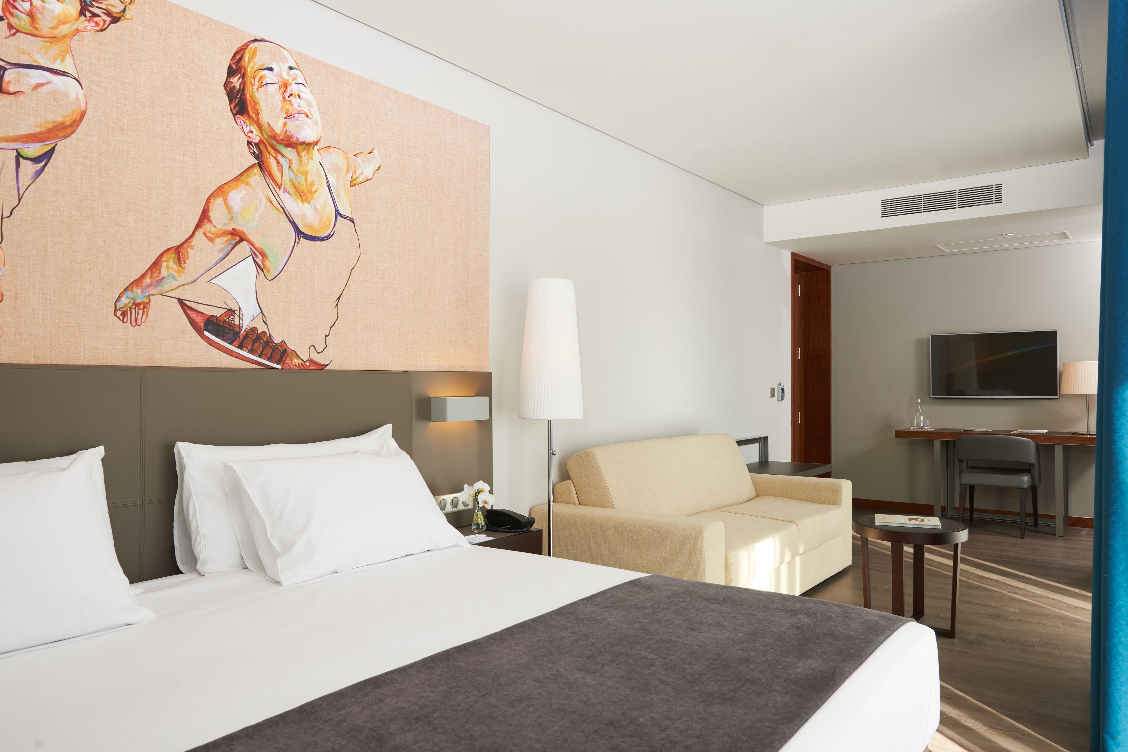 Ein Hotelzimmer mit einem großen Bett, einer Couch, einem Schreibtisch und einem Fernseher.