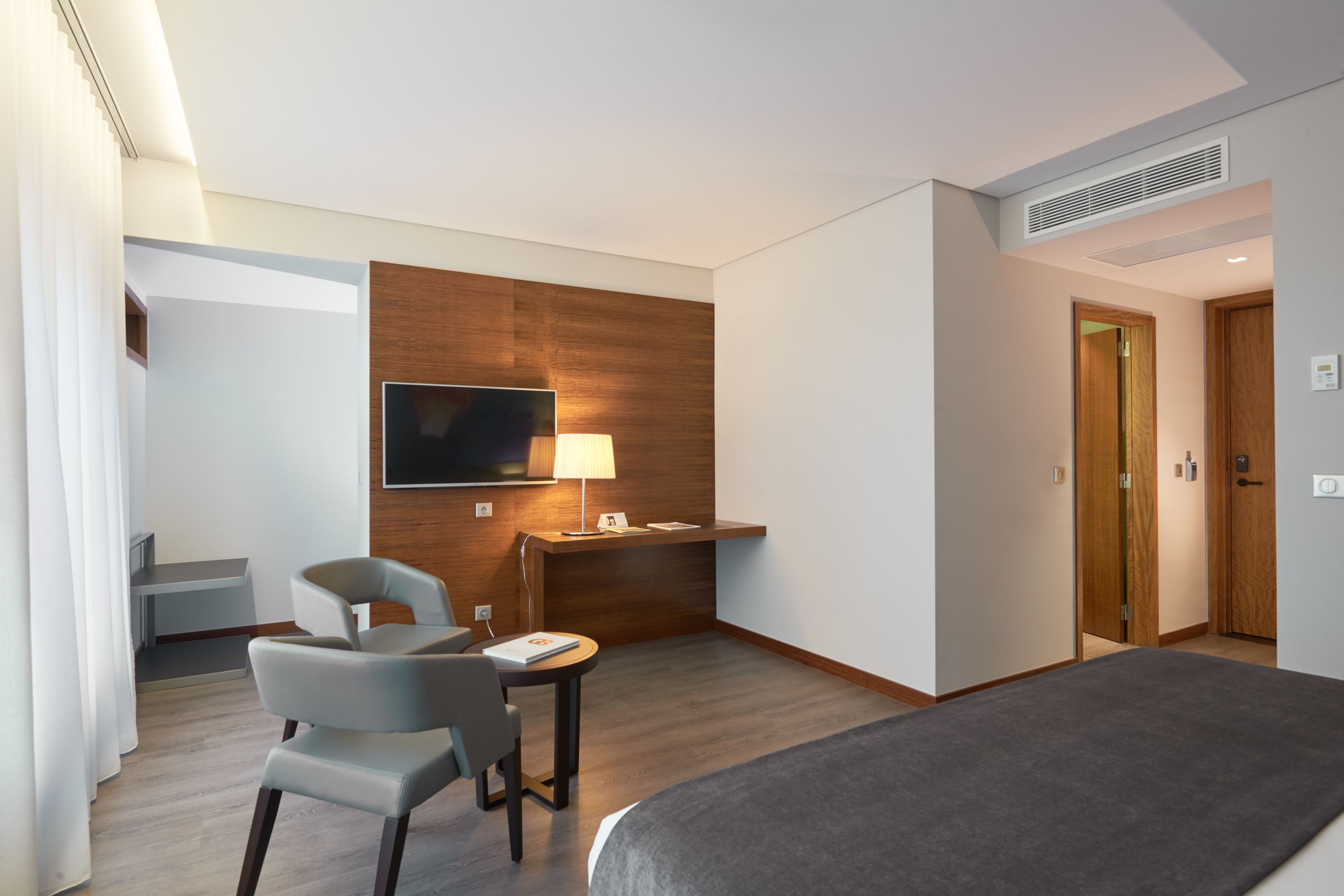Una habitación de hotel con una cama, un escritorio con lámpara, una silla y un televisor instalado en la pared.