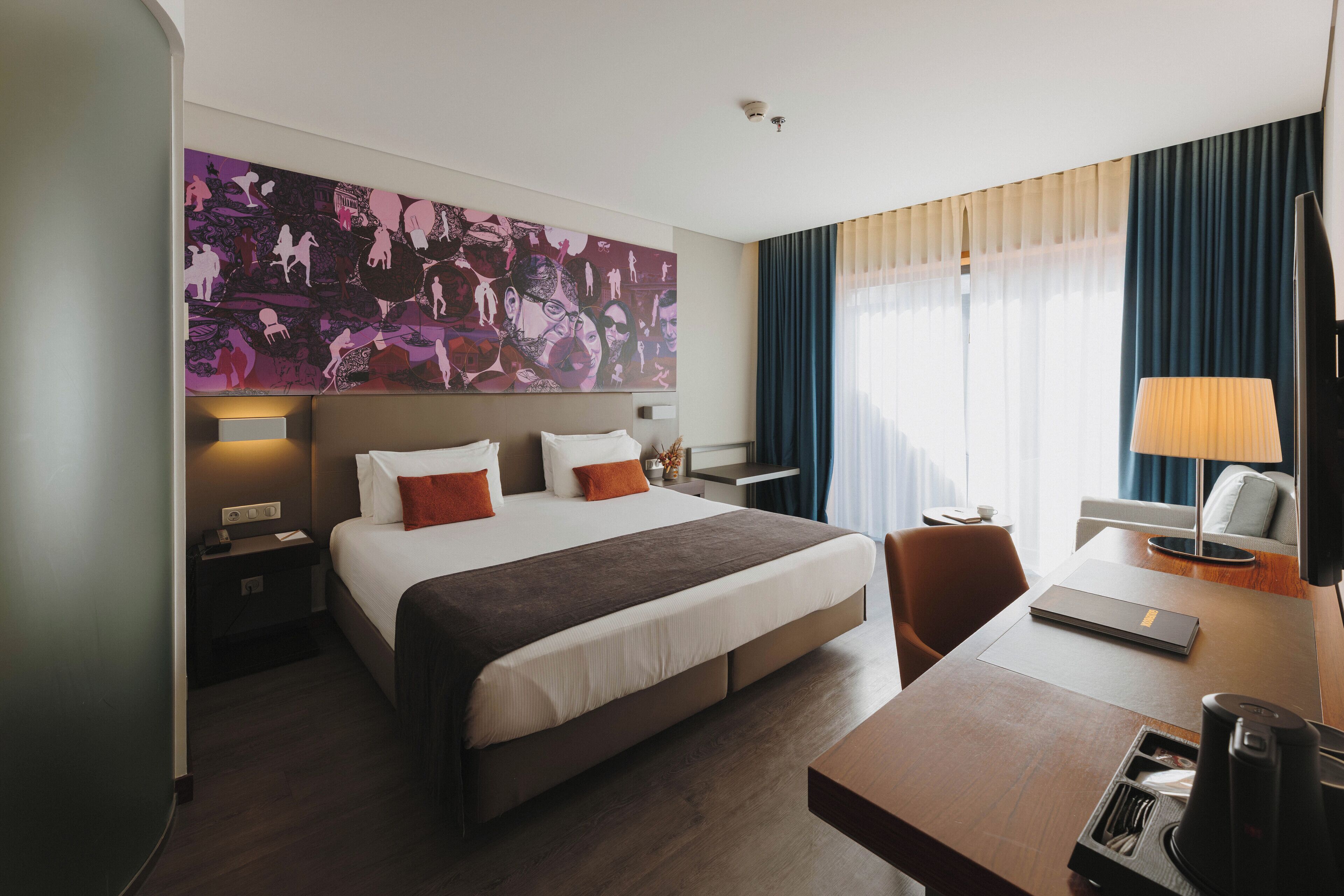 A hotel room with a large bed, a desk with a lamp, a chair, a coffee maker, and a painting on the wall.