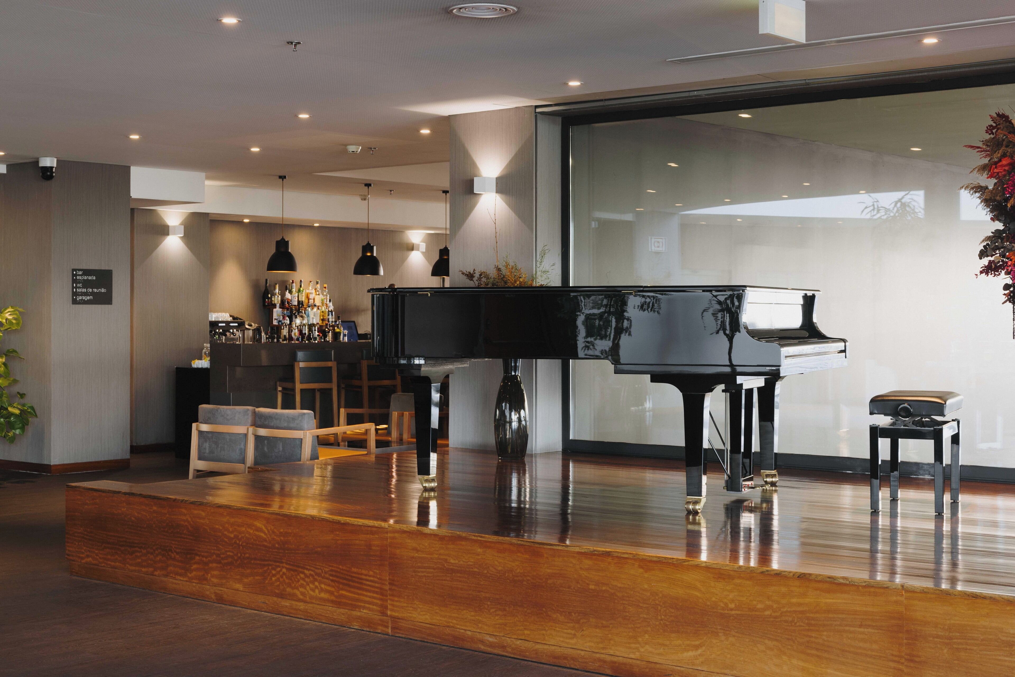 A modern interior with a grand piano, wooden flooring, and a bar area.