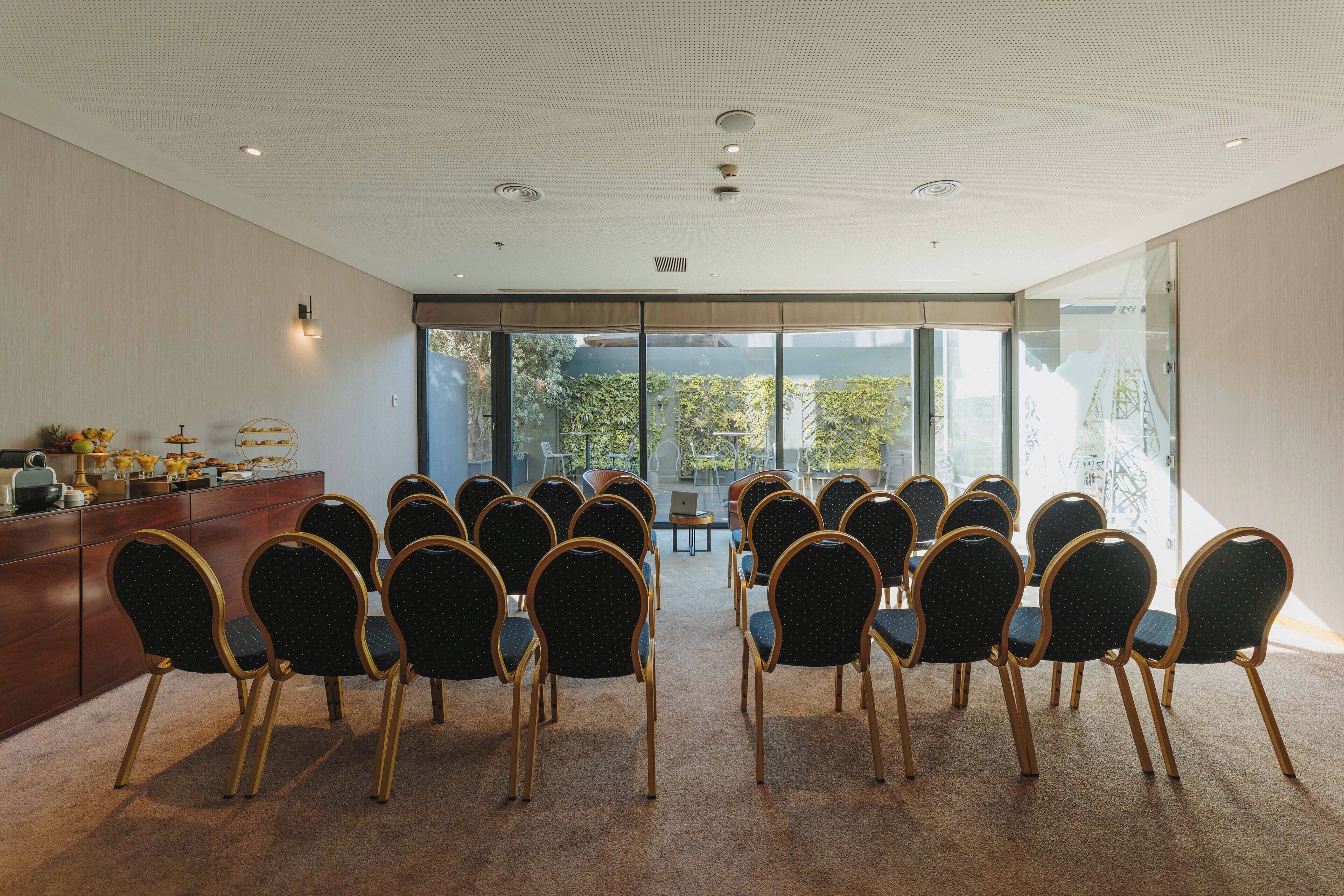 Une salle de conférence avec des rangées de chaises disposées face à une table, de grandes fenêtres et un design moderne au plafond.