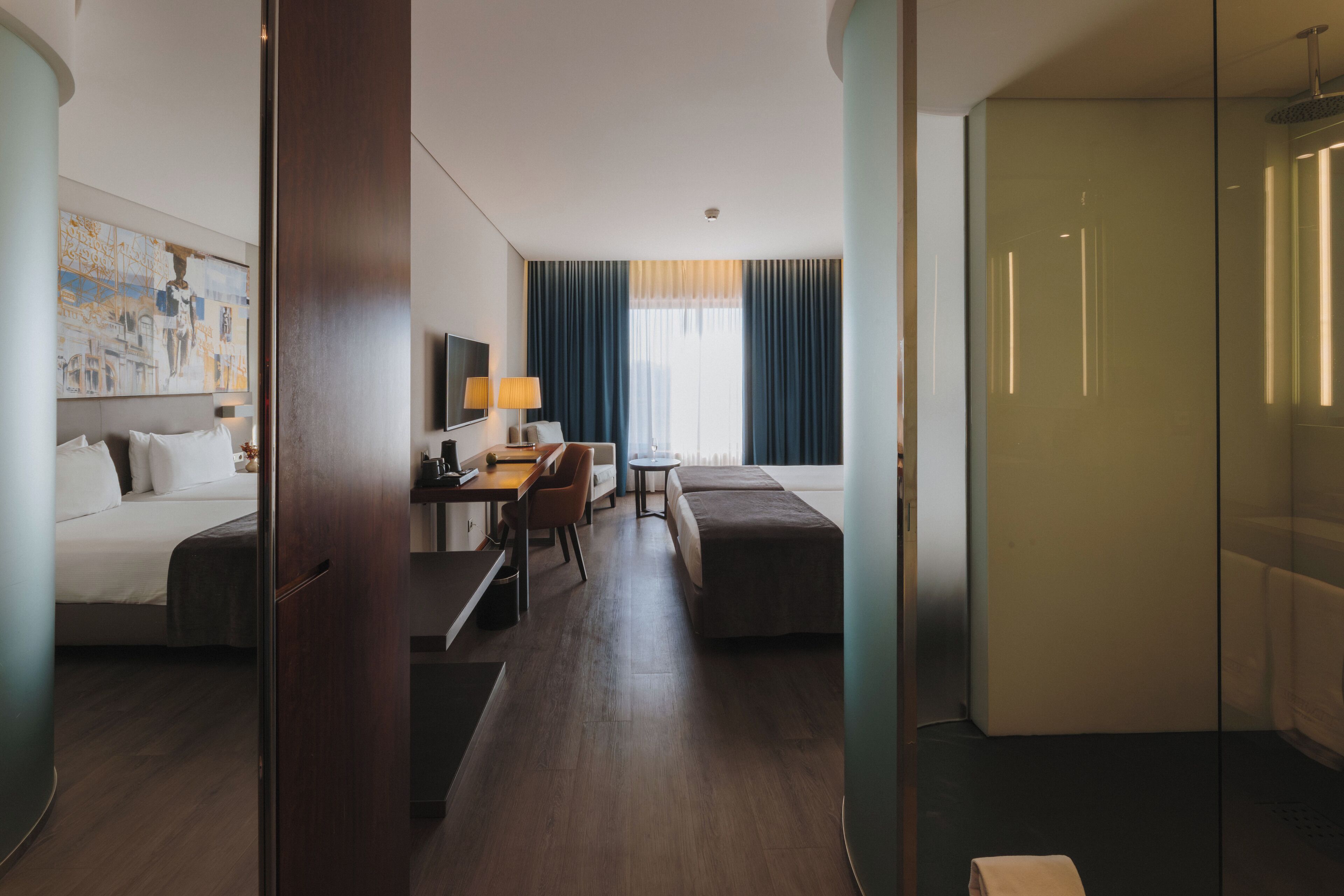Et moderne hotelværelse med seng, skrivebord, stol, sofa og bruseafskærmning i glas.